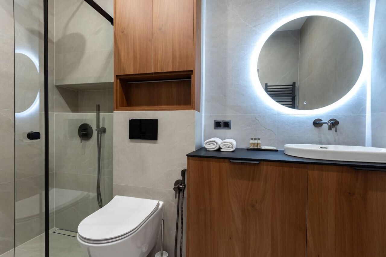 Ein modernes Badezimmer mit Duschkabine aus Glas, einer weißen Toilette, einem hölzernen Waschtisch mit rundem Spiegel und einem Waschbecken.