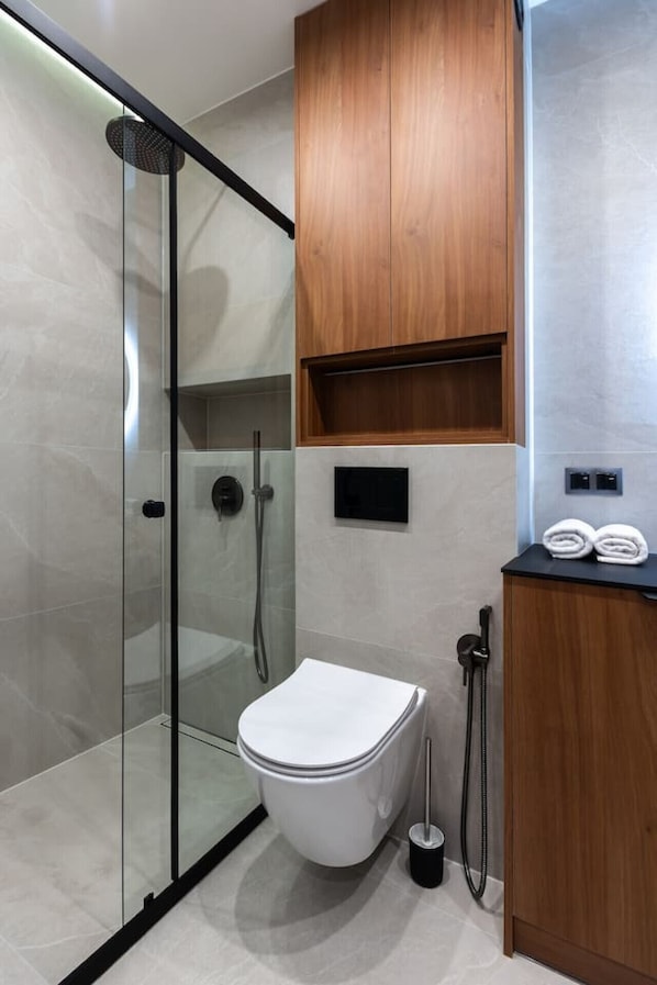 A modern bathroom with a glass-enclosed shower, a white toilet, and wooden cabinetry.