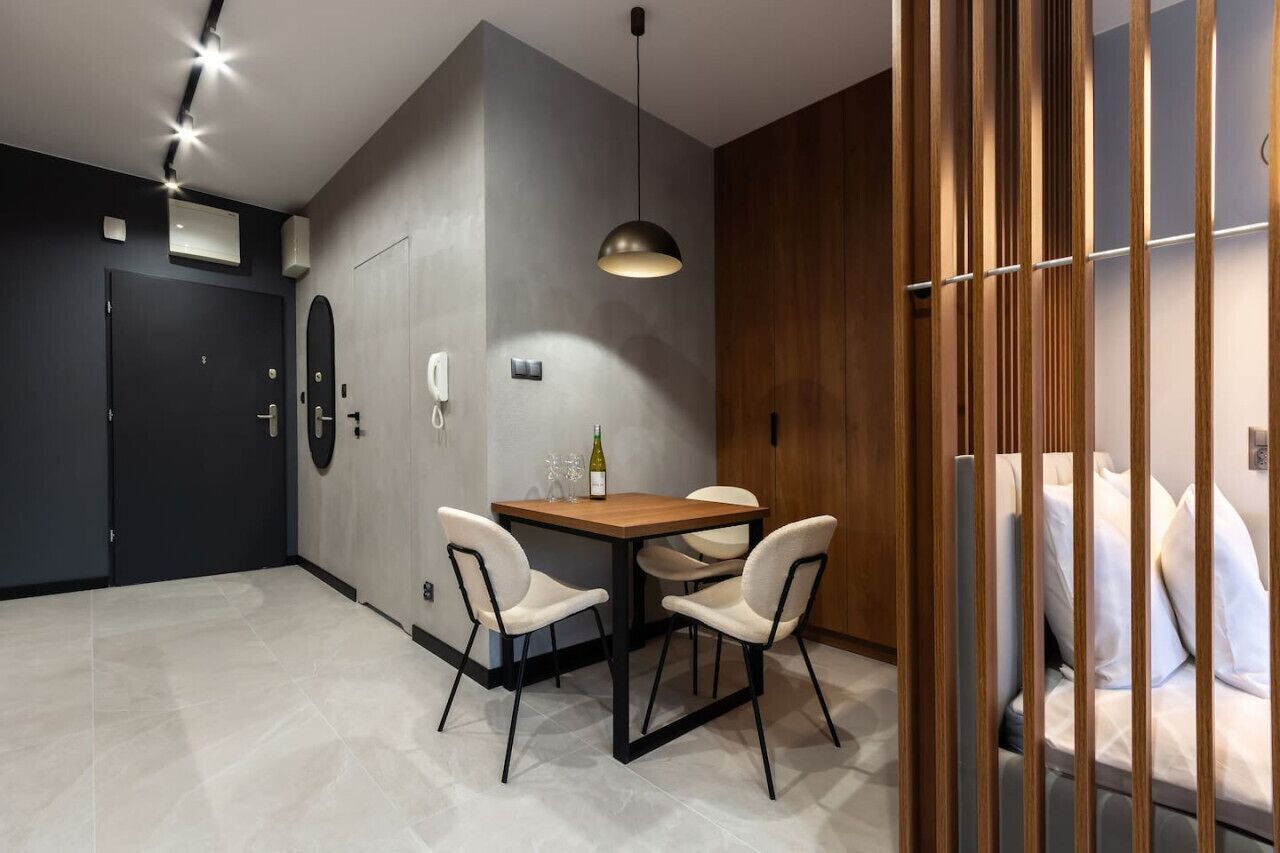 A modern room with a dining table, chairs, a wooden partition, and a bed with white bedding.