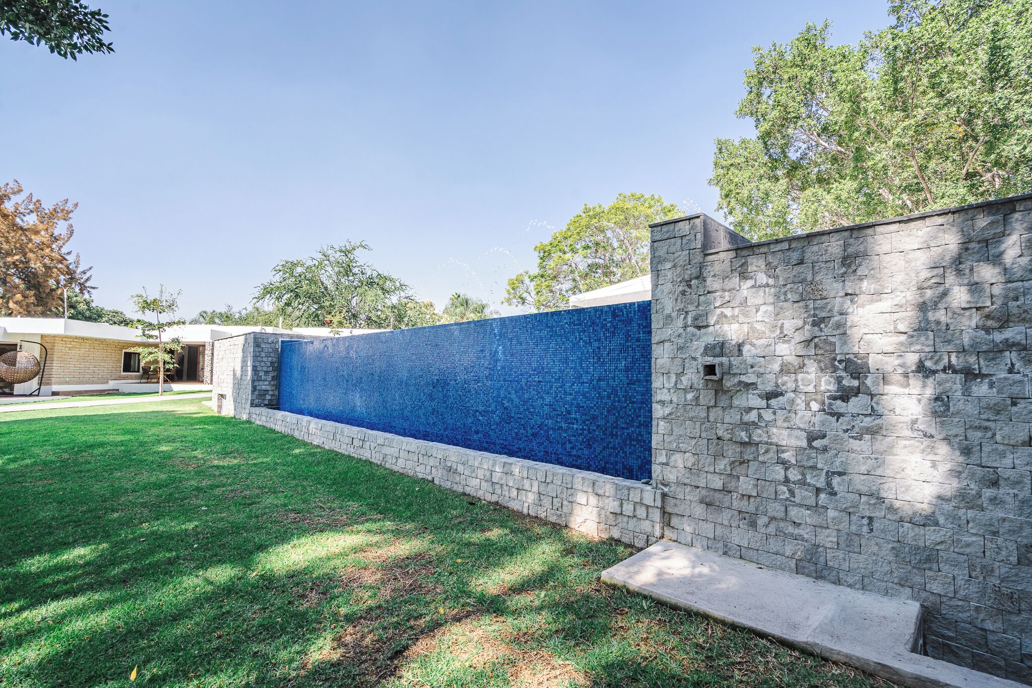 Un espacio exterior moderno con un muro de piedra y una pared de mosaico azul.