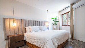 Une chambre moderne avec un grand lit, une table de chevet en bois et une plante en pot.