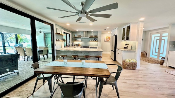 A modern kitchen with a central island, bar stools, and a dining table with chairs.