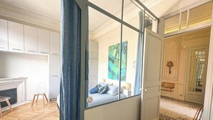 Quarto com cama, uma cadeira, lareira e uma janela grande com cortinas.