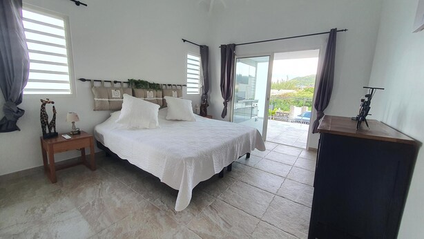 A bedroom with a bed, a nightstand, a desk, and a view of the outside.