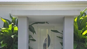 A modern building entrance with a glass door, a doormat labeled "HOME", and large green plants on either side.