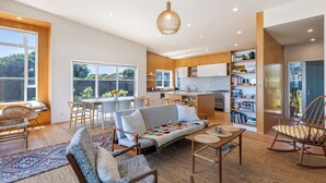 Un vaste espace de vie comprenant un canapé, une table basse et des fauteuils, une cuisine avec des meubles en bois, et un coin repas avec une table et des chaises.