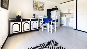 Una cocina compacta con armarios blancos, una mesa azul y dos sillas blancas.