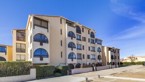 Un edificio de varios pisos con balcones, un estacionamiento y un cielo despejado.