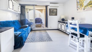 Un espacio habitable pequeño con un sofá azul, una mesa de comedor con sillas, un tapete estampado y una puerta que da a un área exterior.