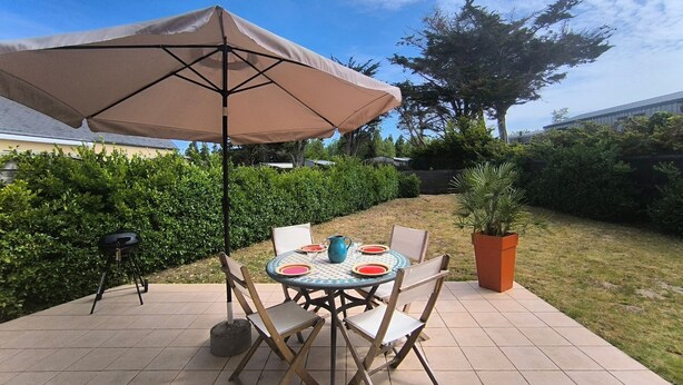 Eine Terrasse im Freien mit Tisch, Stühlen, einem großen Sonnenschirm und einem Blumentopf.