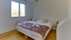 A bedroom with a large bed, two windows, a radiator, and a lamp on a side table. - Arthur - Appt pour 6 avec jardin partagé (Bruz)