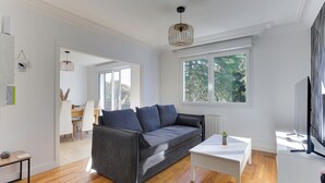 A modern living room with a grey sofa, a white coffee table, and a TV on a white stand. - Arthur - Appt pour 6 avec jardin partagé (Bruz)