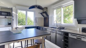 A modern kitchen with a central island, built-in appliances, and large windows. - Arthur - Appt pour 6 avec jardin partagé (Bruz)