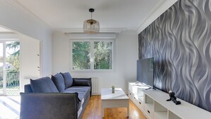 A modern living room with a grey sofa, a white coffee table, and a TV on a white stand. - Arthur - Appt pour 6 avec jardin partagé (Bruz)