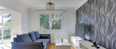 Un salon moderne avec un canapé gris, une table basse blanche et un téléviseur posé sur un meuble blanc.