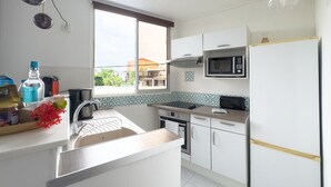 A modern kitchen with white cabinets, a stainless steel sink, a microwave, and a refrigerator. - Ti Arums - Appt climatisé vue mer (Les Trois-Îlets)