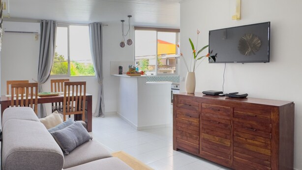 A modern living room with a sofa, dining table, and kitchen area. - Ti Arums - Appt climatisé vue mer (Les Trois-Îlets)