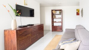 A modern living room with a wooden entertainment center, a grey sofa, and a flat-screen TV mounted on the wall. - Ti Arums - Appt climatisé vue mer (Les Trois-Îlets)