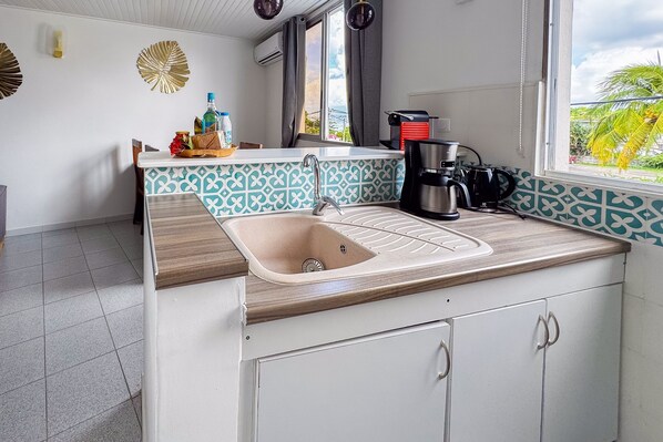 A kitchen with a sink, countertop, and cabinets. There is a window with a view of palm trees and a balcony.