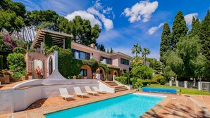 Una piscina con bordeado de baldosas, zona cubierta y un edificio con patio y escalera.