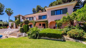 Una casa de dos pisos con un césped cuidado, una piscina y un jardín con diversas plantas y flores.