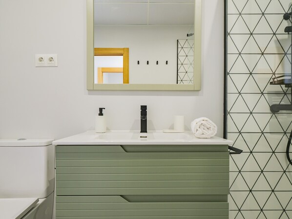 Un baño con lavamanos blanco, tocador verde, un espejo y pared con azulejos.