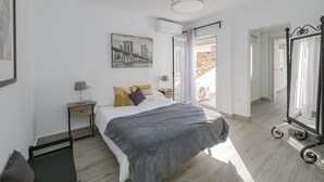 A bedroom with a bed, a nightstand, a lamp, a ceiling fan, a large mirror, and a window with curtains.