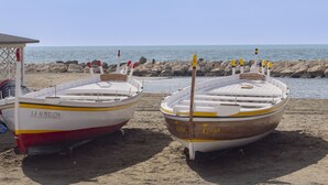 Two boats on a sandy beach with a rocky shoreline and calm sea in the background.