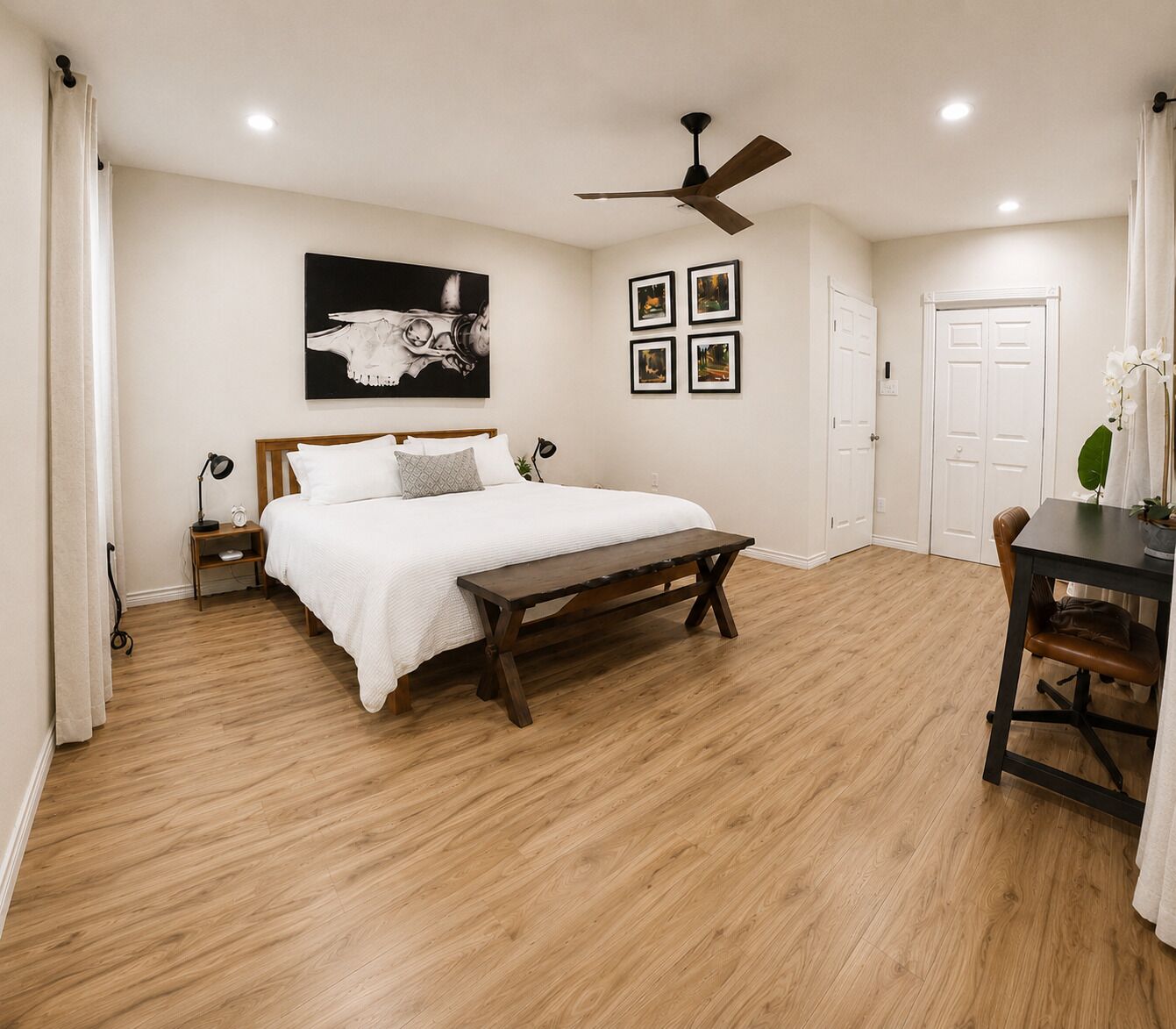 Ein Schlafzimmer mit Holzboden, einem Bett mit weißer Bettwäsche, einem Deckenventilator und einem an der Wand hängenden Bild.