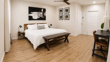 Ein Schlafzimmer mit Holzboden, einem Bett mit weißer Bettwäsche, einem Deckenventilator und einem an der Wand hängenden Bild.
