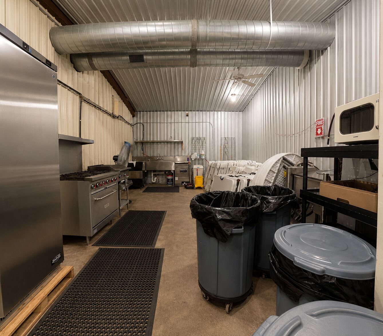 Una cocina comercial con electrodomésticos de acero inoxidable, sistema de ventilación y contenedores de almacenamiento.
