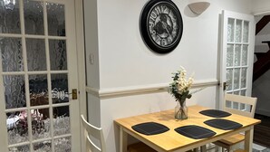 Comedor con mesa de madera, cuatro sillas, un florero con flores y un reloj de pared.