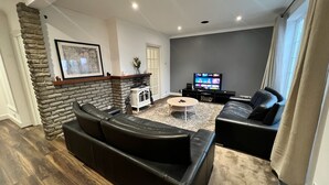 Una sala de estar moderna con chimenea de piedra, sofás de cuero negro, un televisor de pantalla plana y una pequeña mesa blanca.