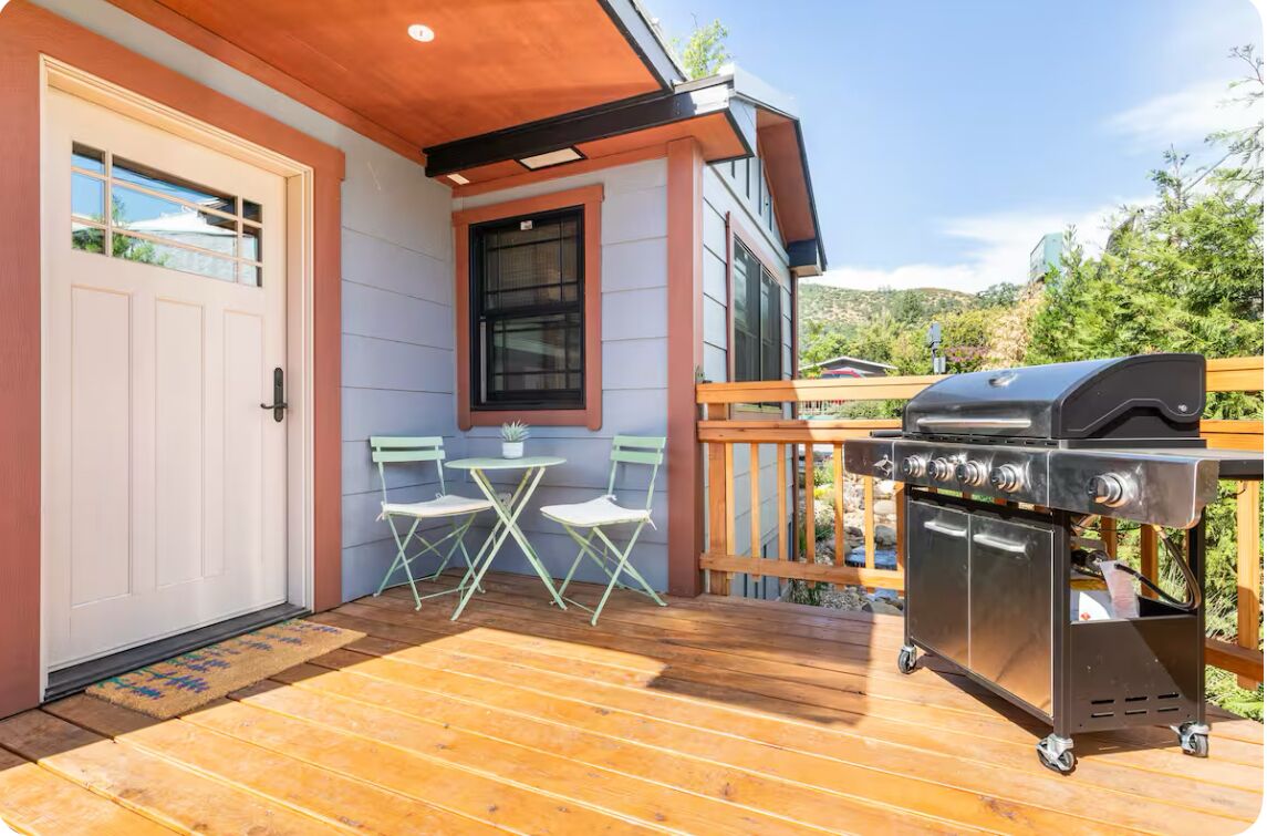 A wooden deck with a barbecue grill, a white door, and a small table with chairs.