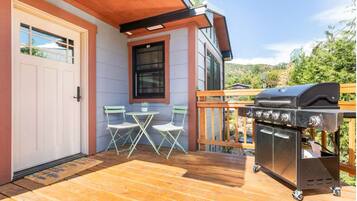 A wooden deck with a barbecue grill, a white door, and a small table with chairs.