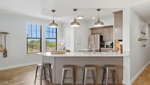 A modern kitchen with a large island, pendant lights, and a view of the outdoors.