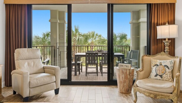 A room with a sliding glass door leading to a balcony with outdoor furniture and palm trees.