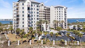 A multi-story hotel with balconies, a parking area, and a view of the sea.