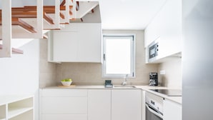 Una cocina moderna con armarios blancos, una escalera de madera, un ventanal y un horno empotrado.