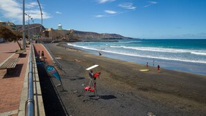 Una playa con paseo marítimo, bancos y silla de socorrista.