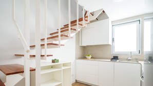 Una cocina moderna con armarios blancos, una escalera de madera y un ventanal que aporta luz natural.