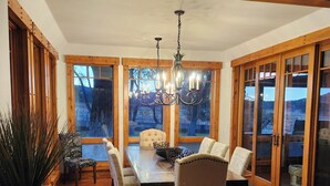 A dining area with a wooden table and chairs, a chandelier, and large windows with a view of the outdoors. - Charming unique 2-bdrm farmhouse in Mesa with WiFi, close to Powderhorn Ski Area (Mesa)