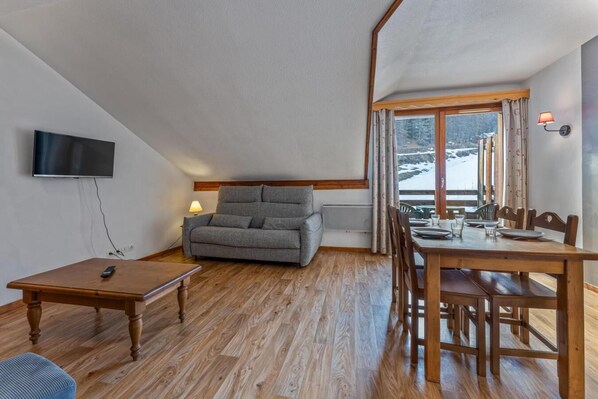 A cozy room with a sofa, a dining table, and a TV mounted on the wall. - Resort center, 2nd floor, view ski slopes, fitness, swimming pool, sauna, balcony, tv, ski locker (Les Orres)