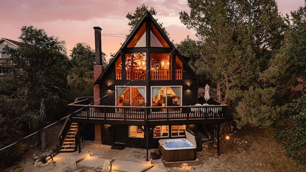 Une cabane à deux étages dotée d’un balcon, d’un bain à remous et d’un espace aménagé avec un foyer.