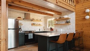 Une cuisine moderne dotée d’un îlot central, de tabourets de bar, de poutres en bois et d’un dosseret de carrelage blanc.