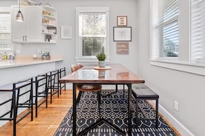 A modern dining area with a long table, black chairs, a patterned rug, and a window with blinds. - Olivia Beach Vacation Home, Sleeps 4-10, Walk to the Beach (Lincoln City)