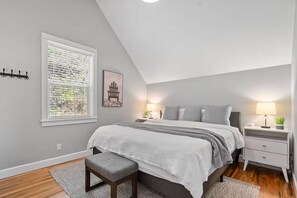 Ein Schlafzimmer mit einem Bett, zwei Nachttischen, einer Bank, einem Fenster mit Jalousien und einem Bild an der Wand.