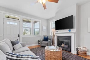 Ein Wohnzimmer mit Sofa, Fernseher, Kamin und Deckenventilator.