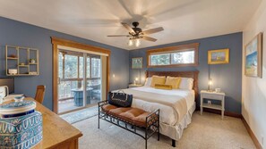 A bedroom with a bed, bedside tables, a desk, a chair, a window, and a ceiling fan.