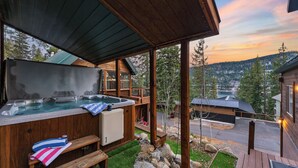 A wooden cabin with a hot tub, a covered deck, and a view of a lake and mountains. - Denton by Avantstay Hot Tub, Deck w/ Fire Pit Near Skiing & Lake! (Truckee)